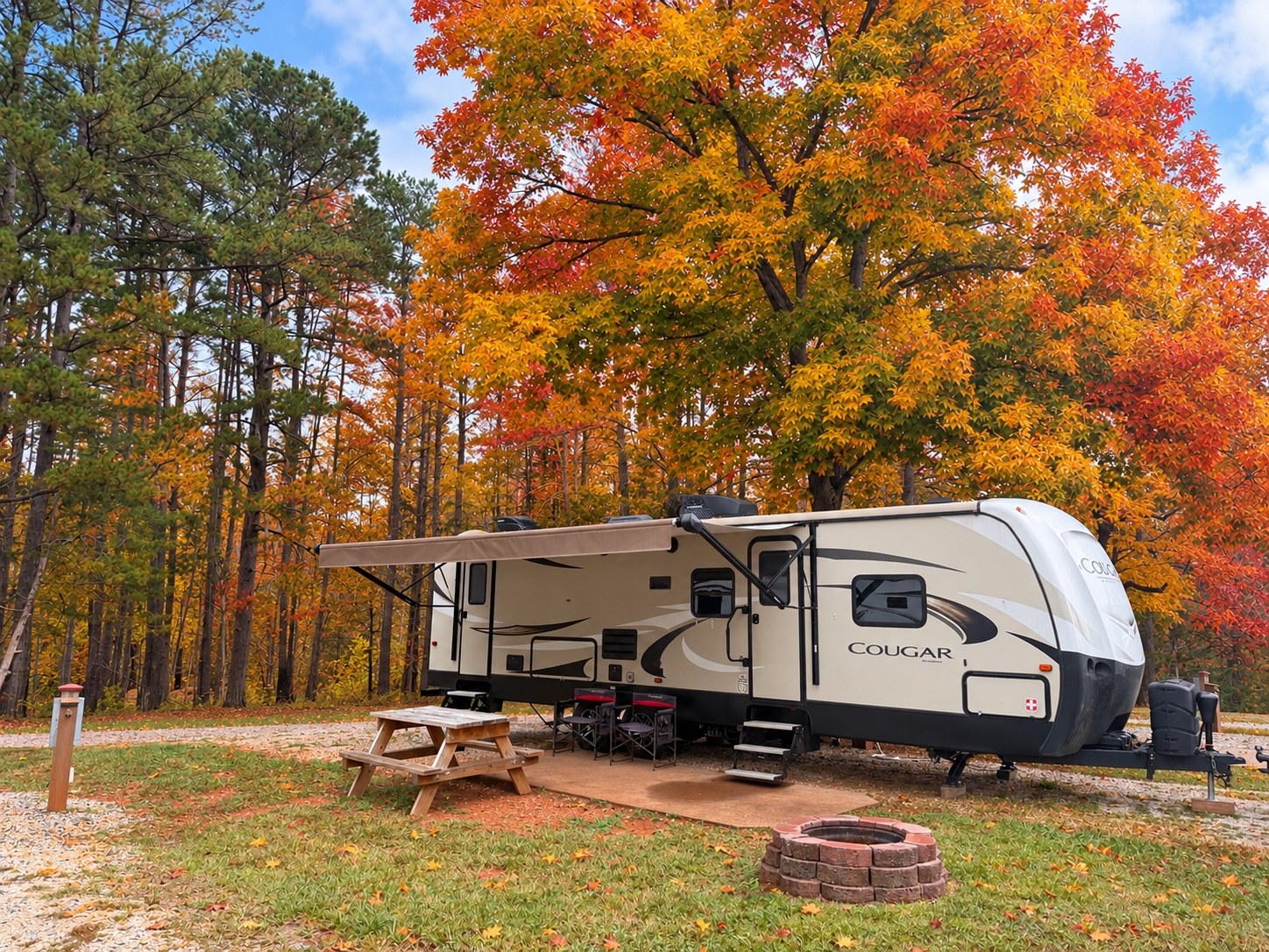 Keystone Cougar camper set up beneath colorful fall trees